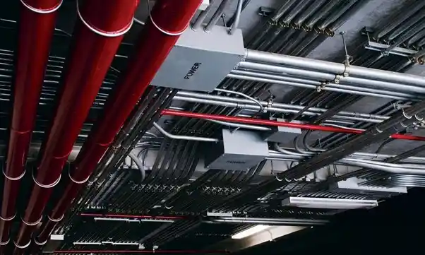 MEP Pipework and Building Systems Overhead MEP pipework with red fire protection pipes, electrical conduits, cables, and other building systems in a ceiling space.